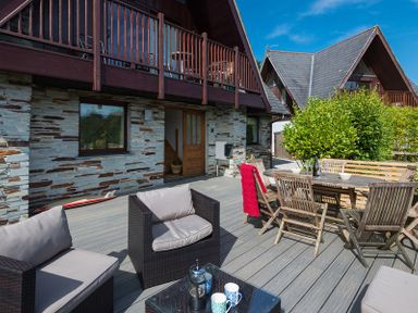 An outdoor patio with cushioned chairs a wooden dining table with chairs and a balcony above at Sandy Hills 8 in Rock