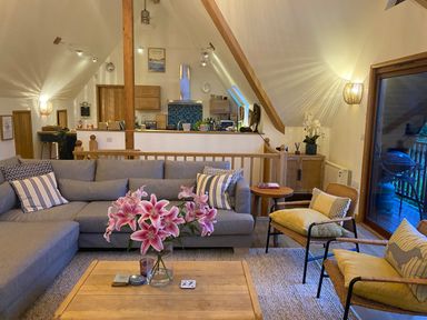 A living room with a gray sectional sofa pink flowers on a wooden coffee table and wooden chairs at Sandy Hills 8 in Rock