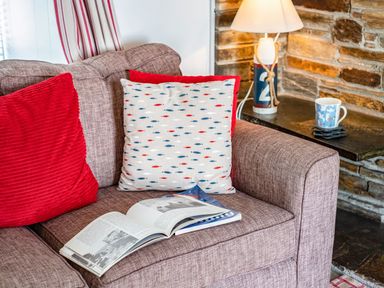 A sofa with cushions and an open book next to a side table with a lamp and a cup at St Michaels in Rock