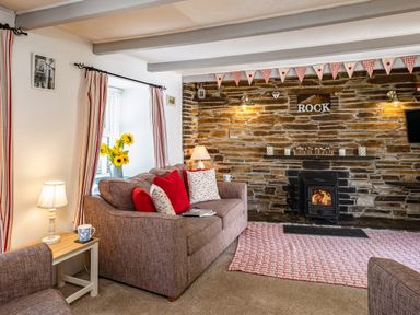 A living room with a sofa red and white cushions a wood burning stove and stone wall at St Michaels in Rock