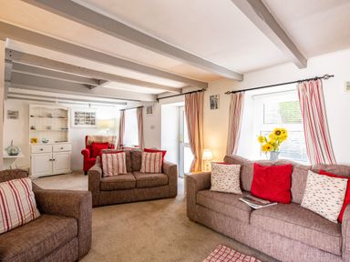 A living room with brown sofas, red and striped cushions, a red armchair, a white cabinet, a lamp, and a window with striped curtains at St Michaels in Rock