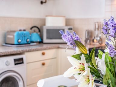 A kitchen counter with a blue toaster and kettle a microwave and flowers on a table at St Michaels in Rock