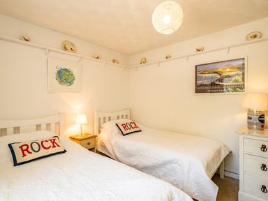 A bedroom with two single beds each with a pillow reading rock and wall art above at St Michaels Rock