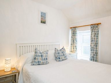 A bedroom with a white bed two patterned pillows two bedside tables with lamps and a window with curtains at St Michaels in Rock