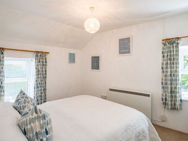 A bedroom with a bed white bedding patterned pillows two windows with patterned curtains and framed pictures on the wall at St Michaels in Rock