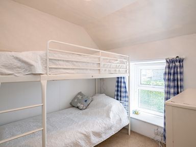 A bedroom with white bunk beds a window with blue check curtains and a white dresser at St Michaels in Rock