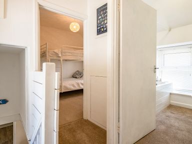 A hallway with a view into a bedroom with bunk beds and a bathroom with a bathtub and window blinds at St Michaels Rock