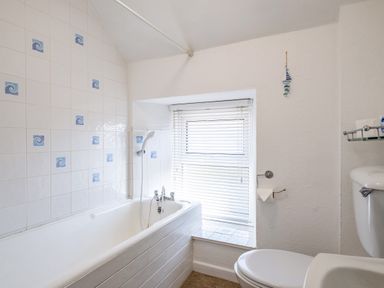 A bathroom with a bathtub a showerhead a toilet a window with blinds and a tiled wall with blue swirl patterns at St Michaels in Rock