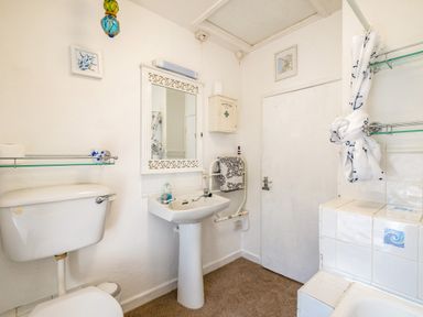 A bathroom with a toilet sink mirror white cabinet and tiled bathtub at St Michaels Rock