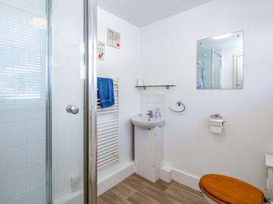 A bathroom with a shower, sink, mirror, wooden toilet seat, and towel rail with a blue towel at St Michaels in Rock