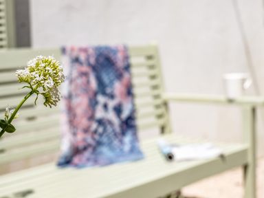 A white flower in focus with a blurred bench holding a colorful cloth a rolled magazine and a white cup in the background at St Michaels in Rock