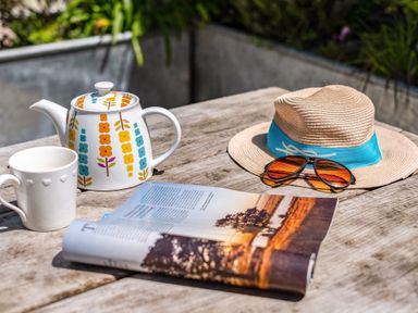 A wooden table with a teapot cup magazine straw hat and sunglasses outdoors at St Michaels in Rock