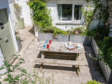 An outdoor patio area with a wooden picnic table and benches surrounded by planter boxes with plants at St Michaels Rock
