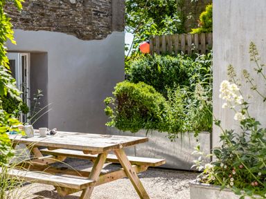 An outdoor patio area with a wooden picnic table and benches surrounded by plants and bushes at St Michaels in Rock