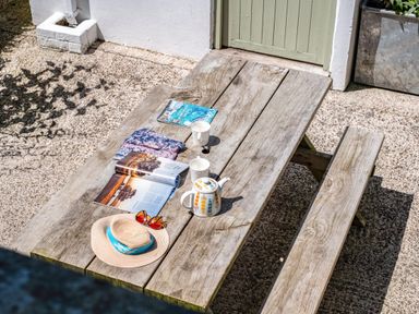 A wooden picnic table outside with two mugs a teapot an open magazine a hat with sunglasses and a folded cloth near a green door at St Michaels in Rock