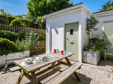 An outdoor patio with a wooden picnic table and benches near a small building with a closed door and potted plants at St Michaels in Rock