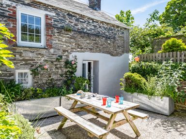 An outdoor patio area with a wooden picnic table and benches outside a stone house with plants and flowers at St Michaels in Rock