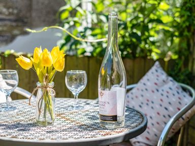 A round metal table with a bottle of wine glasses and a jar of yellow flowers on a patio at St Michaels in Rock