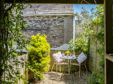 A small outdoor patio with a round metal table and two chairs with cushions surrounded by plants and a stone wall at St Michaels in Rock