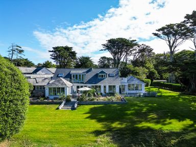 A large house with multiple windows and patios surrounded by a green lawn and tall trees at Greystones in Daymer Bay