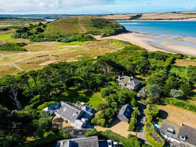 An aerial view of several houses surrounded by trees near a beach and a grassy hill at Greystones in Daymer Bay
