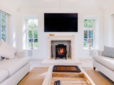 A living room with a fireplace a large tv two sofas and windows at Greystones in Daymer Bay