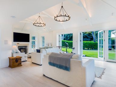 A living room with white sofas a fireplace a television and open doors to a garden at Greystones in Daymer Bay