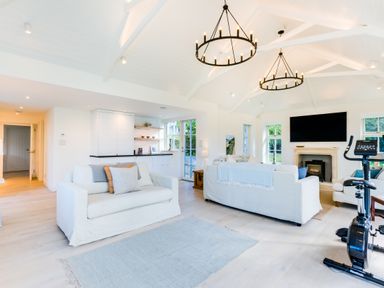 A living room with white sofas a fireplace a large television and exercise bike at Greystones in Daymer Bay