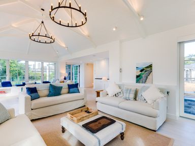 A living room with two beige sofas with cushions a coffee table with trays and large windows at Greystones in Daymer Bay