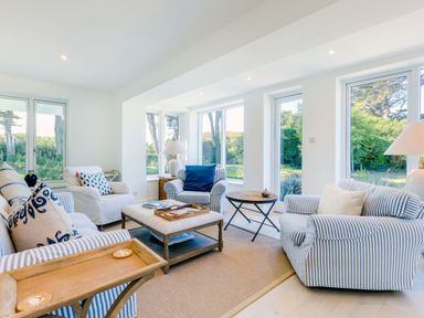 A living room with striped armchairs a white armchair a wooden coffee table and large windows showing greenery outside at Greystones in Daymer Bay