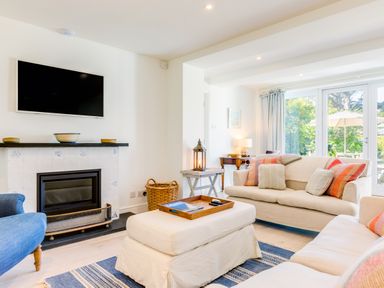 A living room with sofas, a fireplace, a wall-mounted television and a large window at Greystones in Daymer Bay