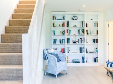 A staircase with carpet next to a white chair and a white bookshelf filled with books and decorative items in a living room at Greystones Daymer Bay