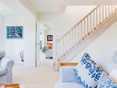 A living room with striped sofas pillows paintings on walls and a staircase at Greystones in Daymer Bay