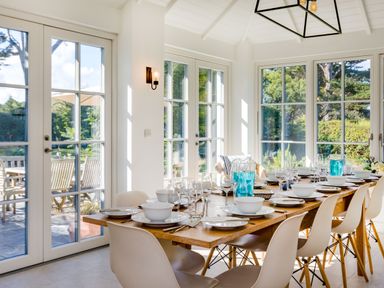 A dining room with a wooden table and chairs set with dishes and glasses at Greystones in Daymer Bay