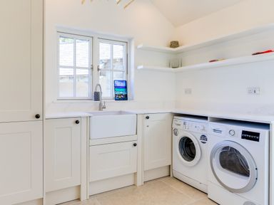A laundry room with two white washing machines a white sink and shelves at Greystones in Daymer Bay