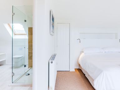 A bedroom with a double bed and a bathroom with a glass shower enclosure visible through an open doorway at Greystones Daymer Bay