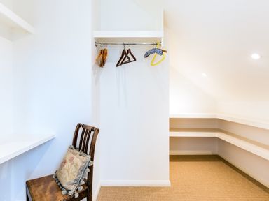 A small room with hangers on a wall rod a wooden chair with a decorative pillow and built in shelves at Greystones in Daymer Bay