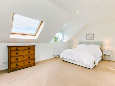 A bedroom with a double bed bedside tables lamps a chest of drawers skylight window and a small window at Greystones in Daymer Bay