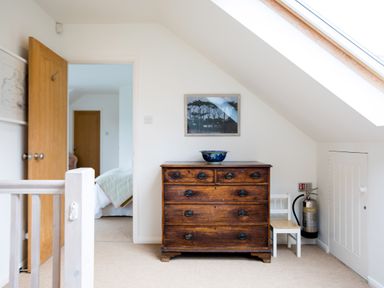A wooden chest of drawers with a blue bowl on top next to a small white chair and a fire extinguisher under a slanted ceiling with a skylight at Greystones in Daymer Bay