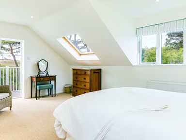 A bedroom with a bed chest of drawers dressing table and chair with windows showing trees