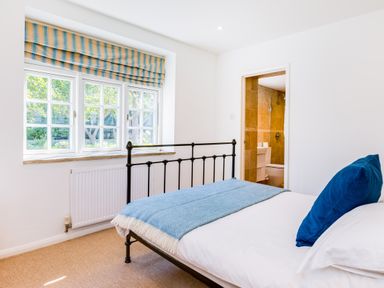A bedroom with a black metal bed frame blue throw blanket and a blue pillow next to a window and an en suite bathroom at Greystones in Daymer Bay