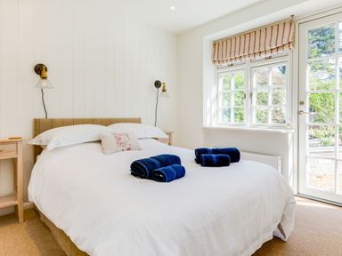 A bedroom with a bed with white linens two bedside tables wall lights and a window with a door at Greystones in Daymer Bay