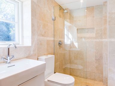 A bathroom with a white sink and chrome faucet a toilet and a glass-enclosed shower with beige tile walls