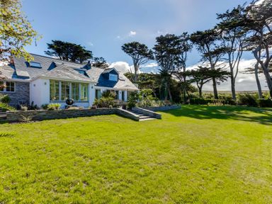 A large green lawn with a stone house and trees in the background at Greystones Daymer Bay