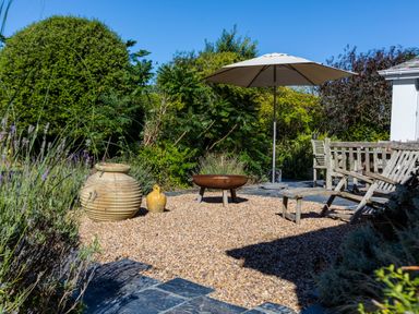 An outdoor garden area with large pots a fire pit wooden seating and an umbrella at Greystones in Daymer Bay