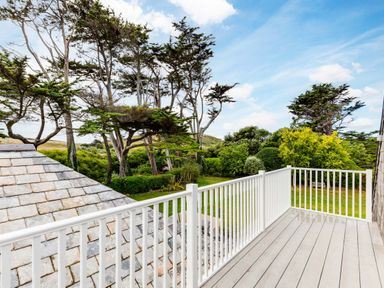 A balcony with white railing overlooking trees and a garden at Greystones in Daymer Bay