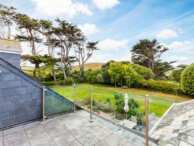 A balcony with glass railing overlooking a garden with lawn trees and outdoor furniture at Greystones in Daymer Bay