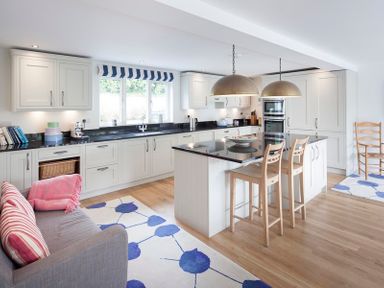 A kitchen with white cabinets a black countertop an island with two wooden stools and a grey sofa with striped cushions at Cherrytrees Rock