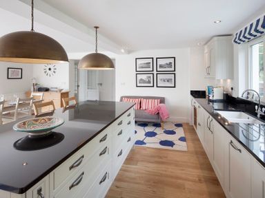 A kitchen with black countertops white cabinets a dining table and a small couch with striped cushions at Cherrytrees in Rock