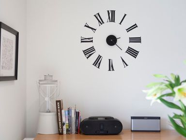 A desk with books a radio and a speaker under a wall clock with Roman numerals at Cherrytrees in Rock